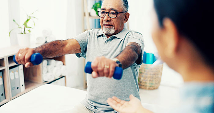 Senior care, exercise and physiotherapist with old man, dumbbell and healthcare at nursing home. Physio, rehabilitation and retirement, fitness coach caregiver and elderly patient mobility training